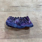 A raw purple crystal cluster geode section with dark blue and violet agate bands, resting on a light brown wooden surface.