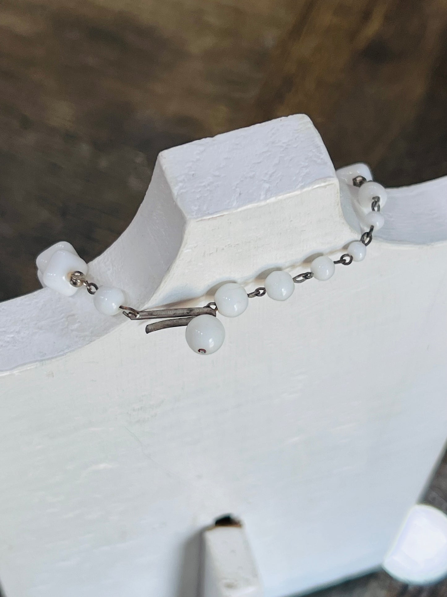 A delicate silver-toned chain bracelet with white round beads draped over a white display stand.