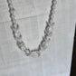 A white beaded necklace with alternating smooth round beads and carved shell-like teardrop beads, displayed on a wrinkled white fabric background.