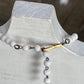 A beaded necklace with white round beads, dark metal links, and a small gold-toned bar detail, displayed on a white jewelry bust.