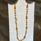 An amber glass bead necklace with teardrop-shaped beads and small round beads, displayed on a white fabric-covered jewelry stand against a dark wooden background.