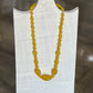 A yellow beaded necklace displayed on a white fabric-covered jewelry stand against a blurred brown wooden background.