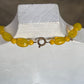 A yellow beaded necklace with a bronze ring clasp displayed on a white jewelry bust.
