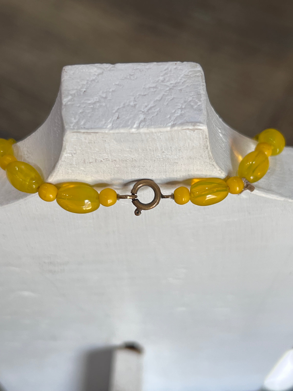 A yellow beaded necklace with a bronze ring clasp displayed on a white jewelry bust.