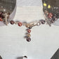 A beaded bracelet with metallic rose gold, copper, and dark bronze pearls, displayed on a white jewelry bust.