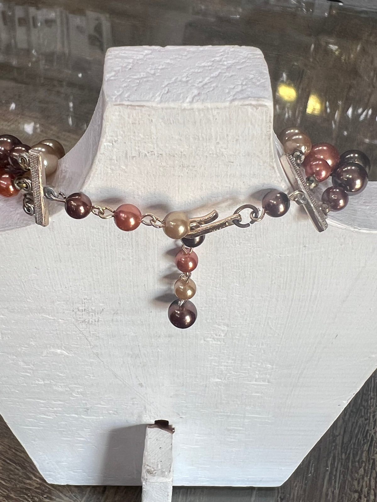 A beaded bracelet with metallic rose gold, copper, and dark bronze pearls, displayed on a white jewelry bust.