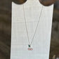 A silver necklace with a cherry pendant displayed on a white fabric jewelry stand against a blurred wooden background.
