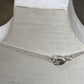 A delicate silver chain necklace with a small heart-shaped charm and clasp, displayed on a white textured mannequin bust.