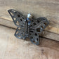 A butterfly-shaped filigree brooch in dark oxidized silver metal, featuring a small clear faceted crystal at the center, resting on a rustic wooden surface.