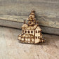 A small wooden house-shaped ornament or charm with laser-burned details, resting on a rustic wooden surface.