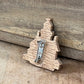 A small wooden Christmas tree-shaped brooch with a silver metal pin back, resting on a rustic wooden surface.