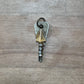 A vintage-style key with a silver-toned metal head and a dangling clear faceted crystal, resting on a light brown wood-grain surface.