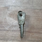 A single vintage metal key with a keyring, photographed on a light brown wood-grain surface.