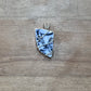 A handmade pendant featuring a light blue and white patterned stone wrapped in silver-colored wire, displayed on a rustic wooden surface.