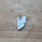 A handmade pendant featuring a light blue-gray irregular stone wrapped in silver-colored wire, resting on a light brown wooden surface.