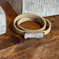 A beige leather wrap bracelet with a rectangular white crystal cluster centerpiece and small gold-tone metal accents, displayed on a rustic wooden surface.