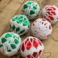6 decorative Christmas ornaments wrapped in white crochet lace over shiny green and red satin balls, arranged on a wooden tabletop.