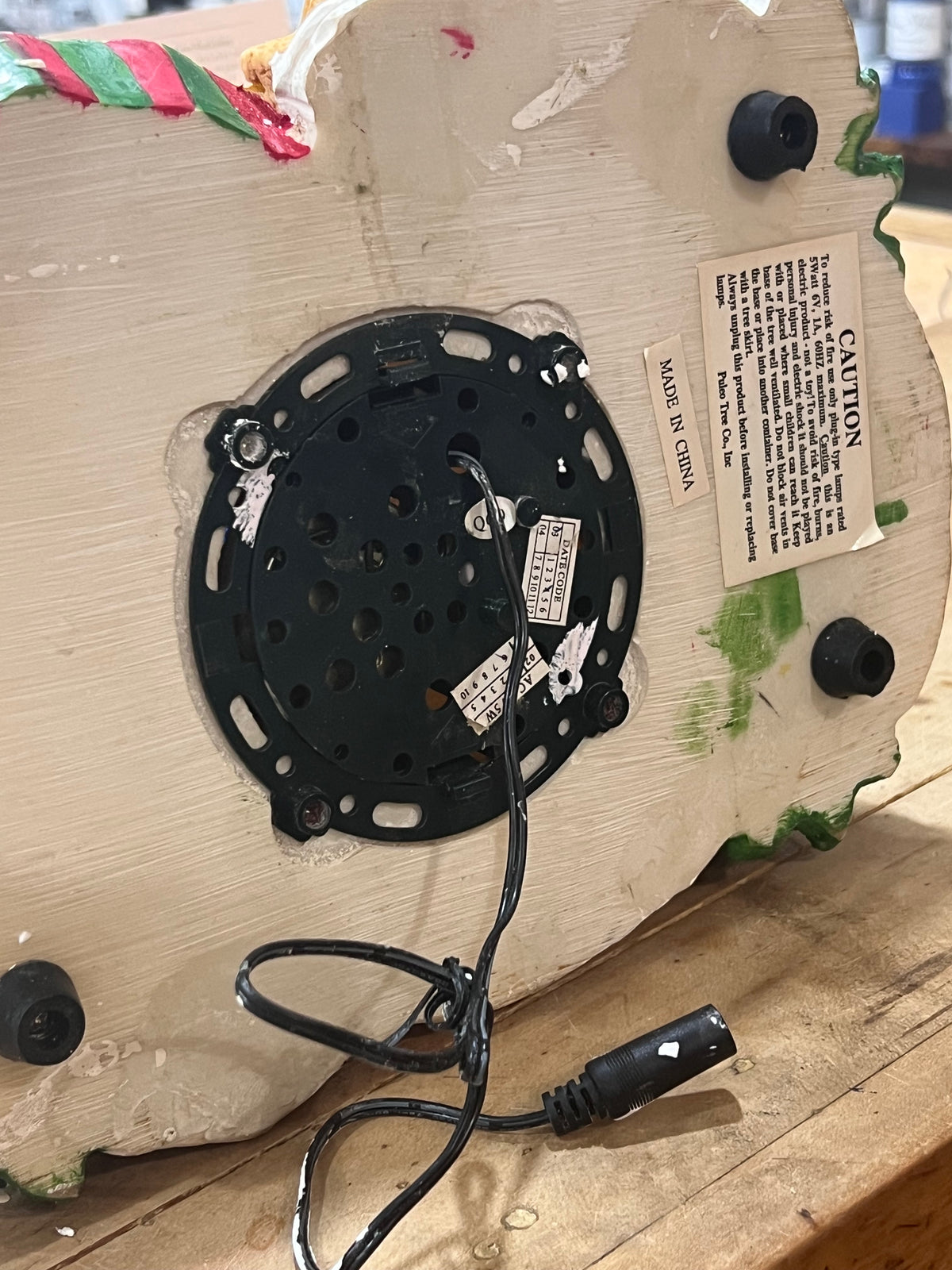 The underside of a vintage wooden appliance, likely a mixer or blender, showing the black motor housing, power cord, mounting feet, and a 'CAUTION' label on a wooden surface.