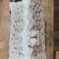 A textured, handcrafted rectangular object with a white and silver glittery surface, featuring a small dark top section with white dots, photographed on a wooden surface.
