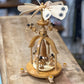 A handcrafted wooden spinning top with decorative painted blades and small figurines, displayed on a rustic wooden workbench.