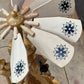 A close-up of a handcrafted wooden spinning wheel with light-colored wooden blades decorated with black floral star patterns, set against a workshop background.