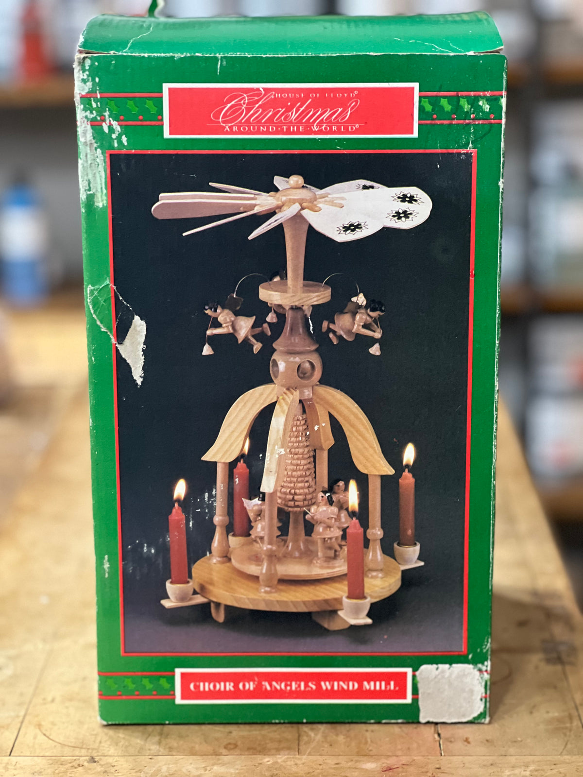 Christmas ornament packaging for a 'Choir of Angels Wind Mill' by Shirklin's, featuring a green box with a photo of the wooden wind mill with lit candles.