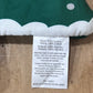 Close-up of a sewn fabric tag on a green and white patterned textile, showing care instructions in English and Spanish on a wooden surface.