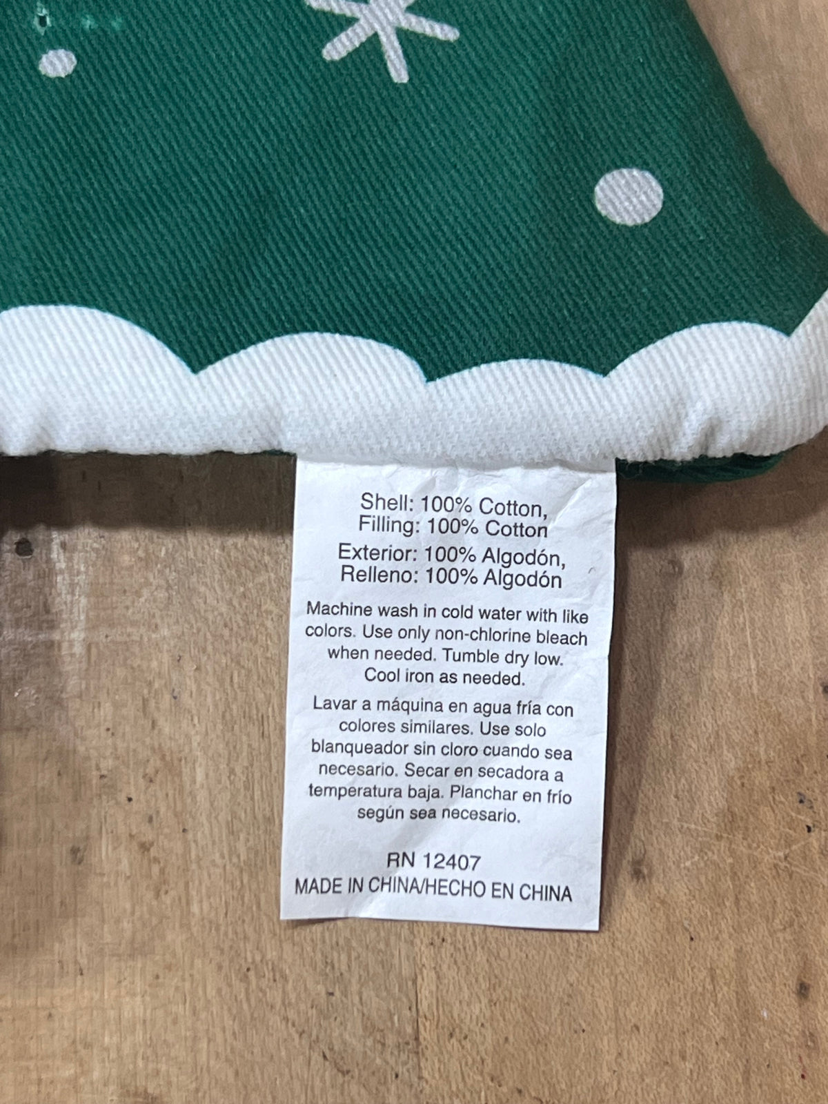 Close-up of a sewn fabric tag on a green and white patterned textile, showing care instructions in English and Spanish on a wooden surface.