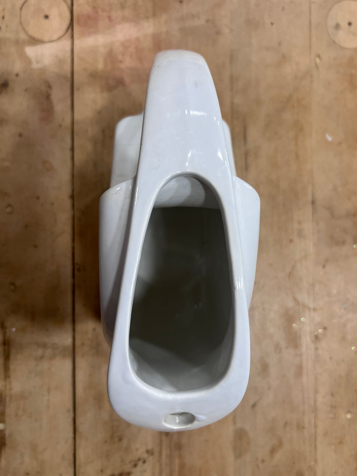 A glossy white ceramic pitcher viewed from directly above, resting on a rustic wooden surface.
