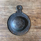 A vintage metal paint strainer with embossed text, resting on a rustic wooden surface.