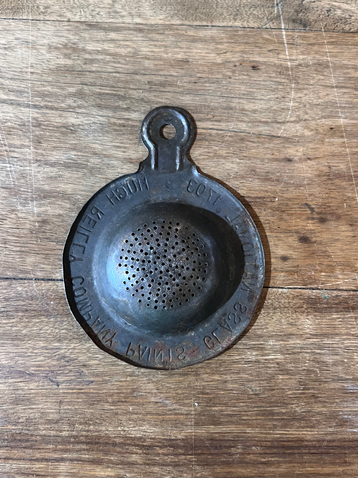 A vintage metal paint strainer with embossed text, resting on a rustic wooden surface.