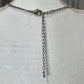 A silver-toned chain necklace displayed on a white textured mannequin bust, featuring a lobster clasp closure and a long dangling heart-link extender chain.