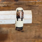 A close-up of a ring with a cream-colored textured band and dark brown marbled stone sections, displayed on a light-colored wooden block over a rustic wooden background.