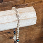 A beaded bracelet with silver-toned beads and dark purple iridescent beads, draped over a light-colored wooden block on a rustic wooden surface.