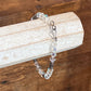 A beaded bracelet with faceted clear and iridescent beads, dark spacer beads, and a silver clasp, displayed on a light wood block over a wooden surface.