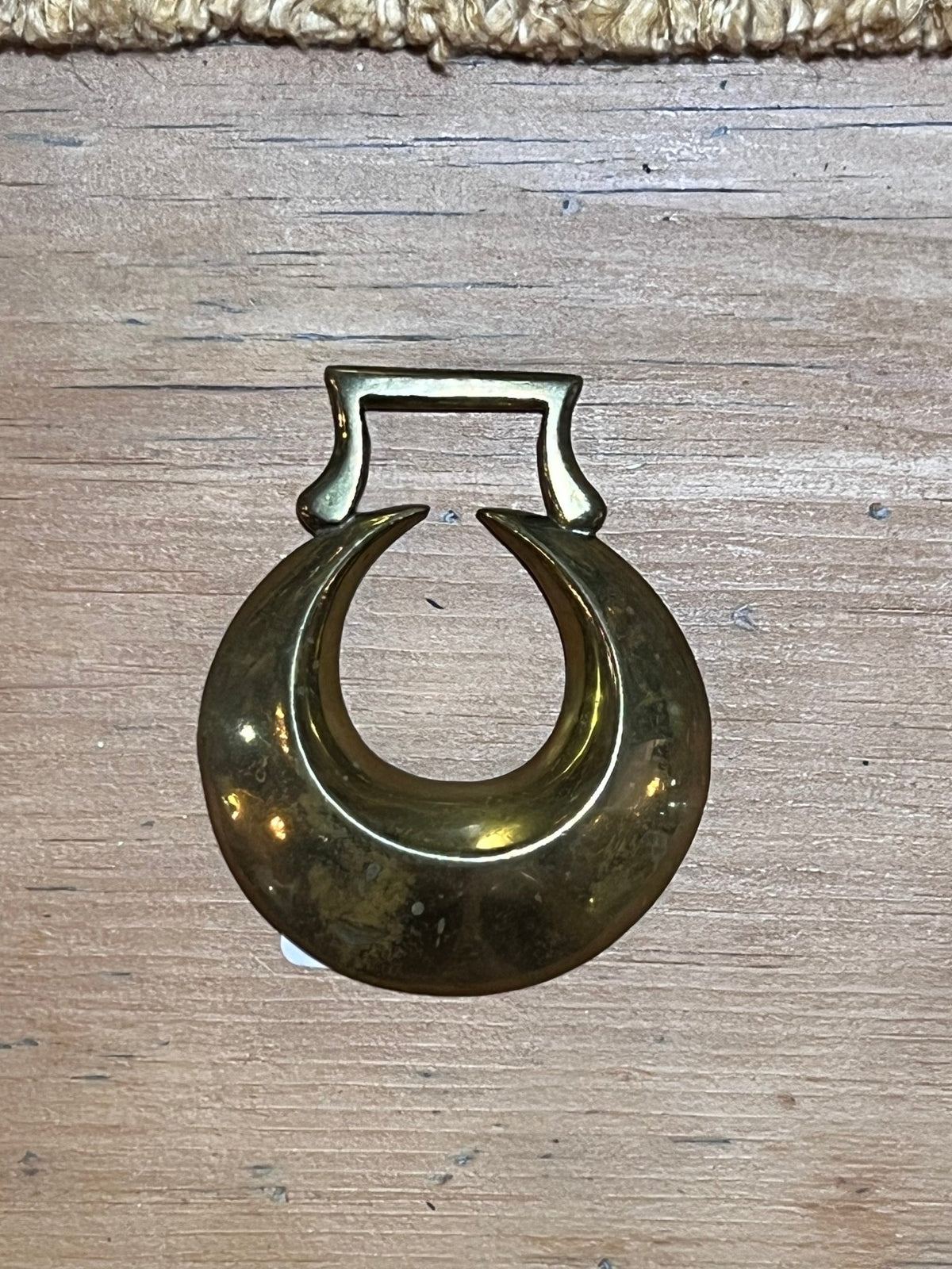 A vintage brass crescent moon ring with a rectangular top, displayed on a light-colored wooden surface.