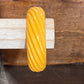 A twisted yellow bangle bracelet displayed on a rustic wooden surface in front of textured gray stone props.