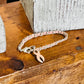 A silver-toned chain bracelet with a pink awareness ribbon charm, displayed on a rustic wooden surface next to a white textured block.