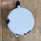 A top-down view of a vintage white enamel mug with a dark blue handle, resting on a light brown wooden surface.