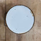 A top-down view of a round metal paint can with a white enamel lid, showing some rust and wear, placed on a rustic wooden surface.