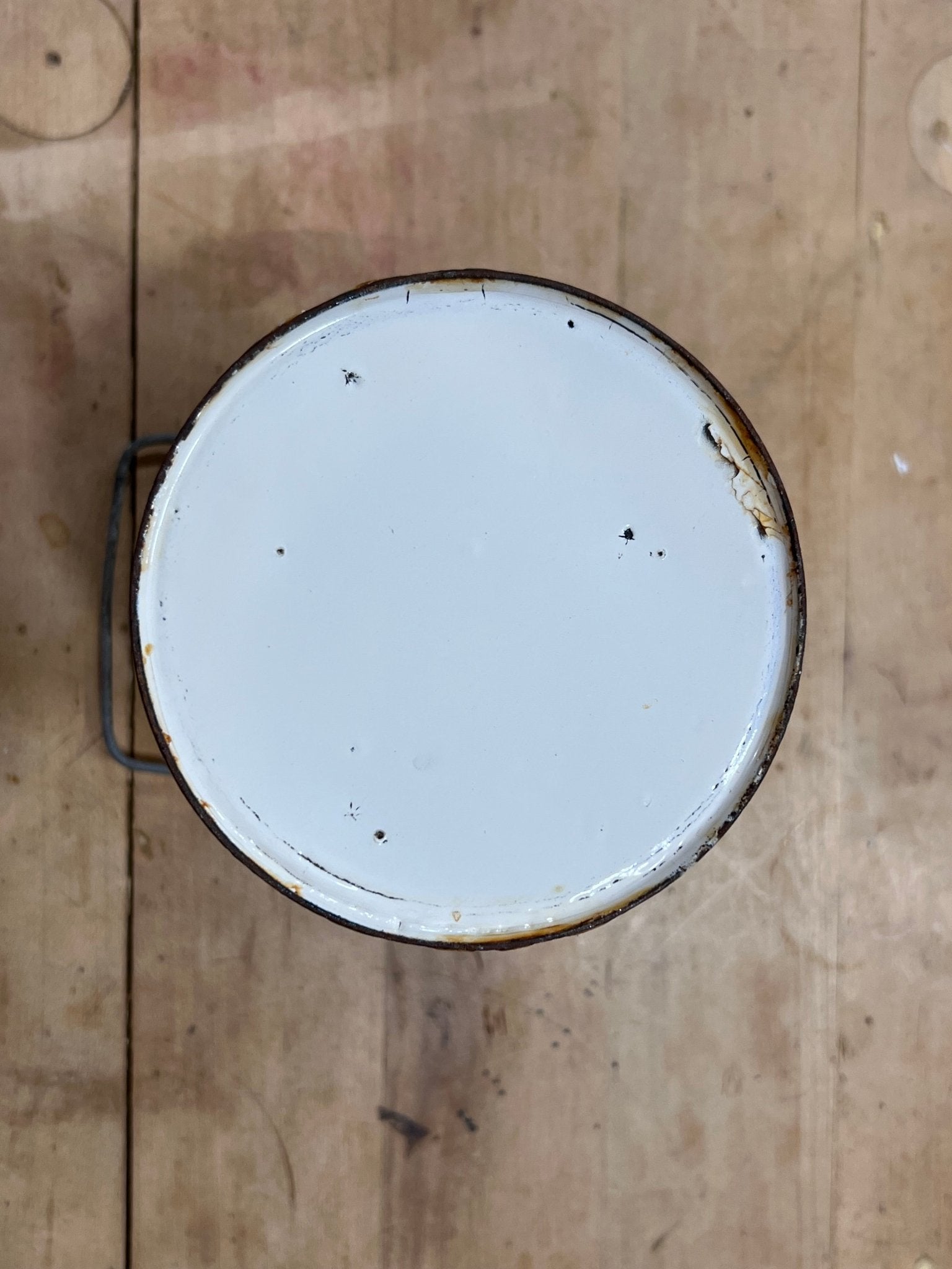 A top-down view of a round metal paint can with a white enamel lid, showing some rust and wear, placed on a rustic wooden surface.