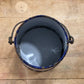 An open metal paint can filled with dark gray paint, viewed from above on a light wood plank surface.