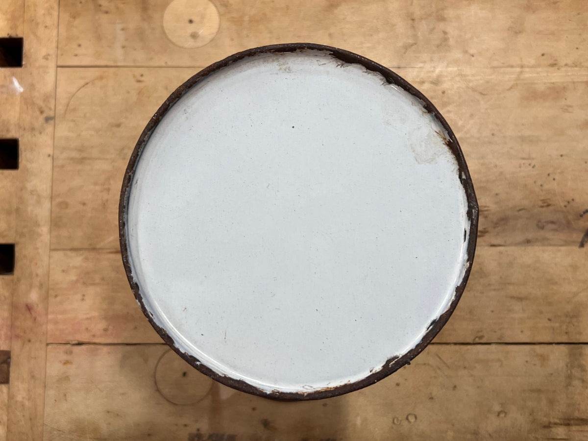 A round white enamel or plastic lid with a dark brown rim, viewed from directly above on a light brown wooden surface.