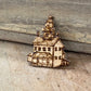 A small wooden house-shaped ornament or charm with laser-burned details, resting on a rustic wooden surface.